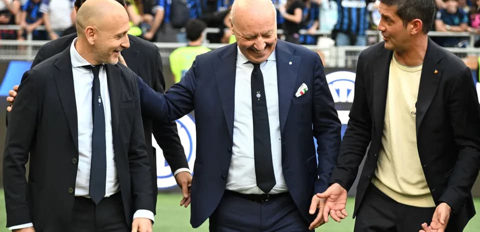 Three men in suits smiling on the pitch