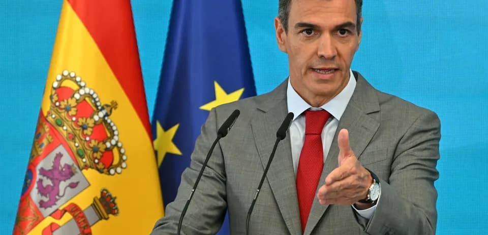 Politician speaking at podium with flags in background