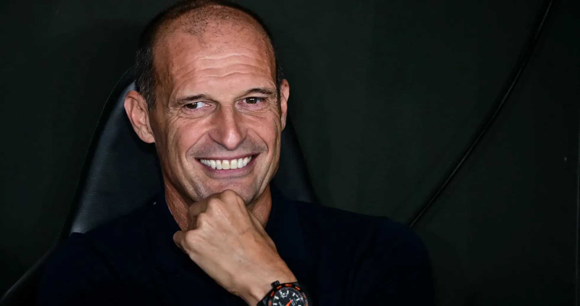 Smiling coach seated with hand on chin