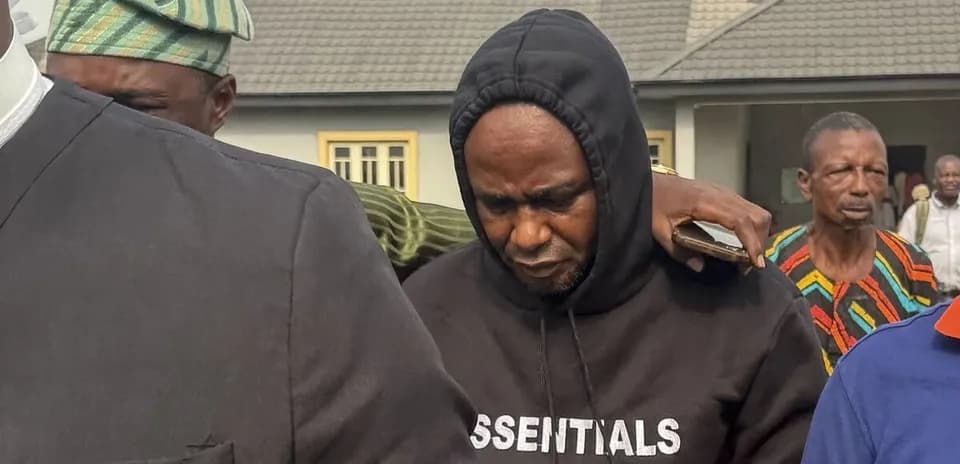 Man in hoodie being escorted by others outdoors