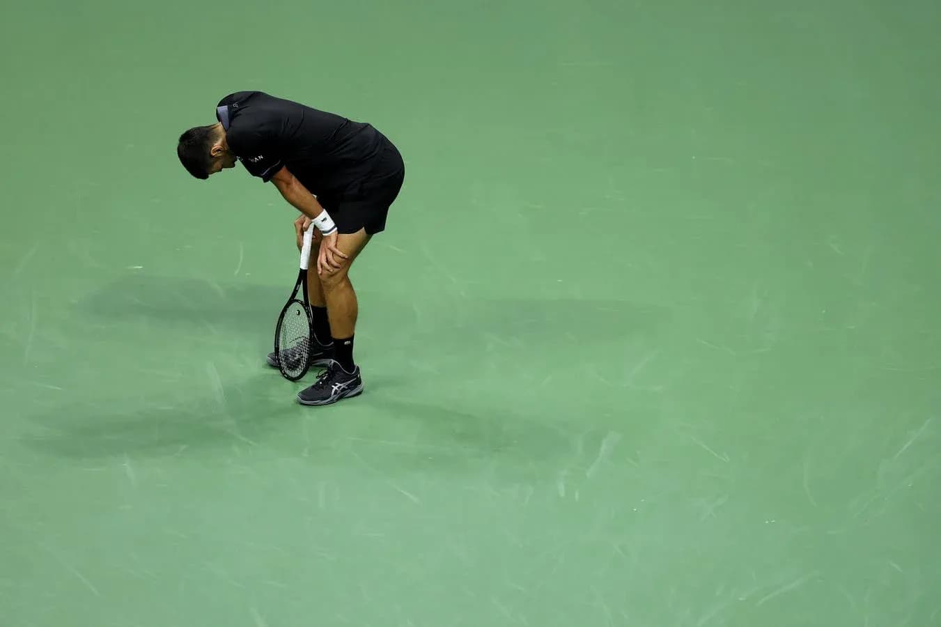 Tennis player bending over on green court