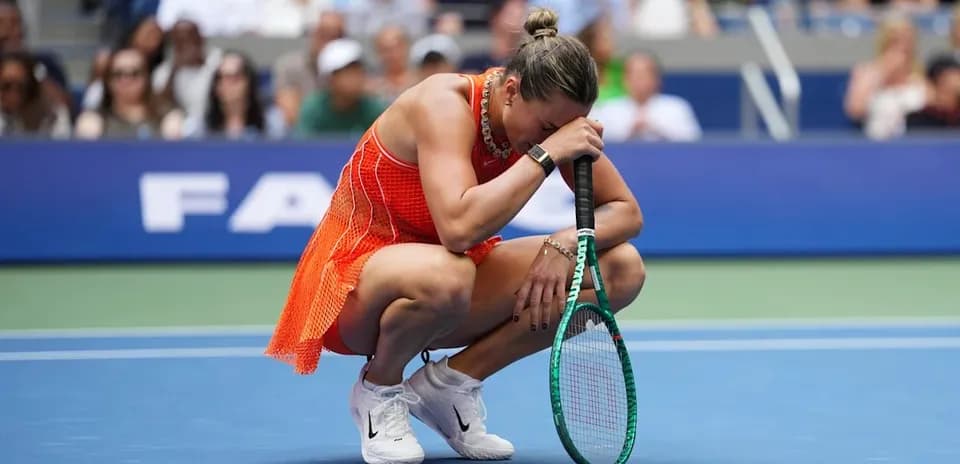 Player kneeling on court holding racket, crowd visible