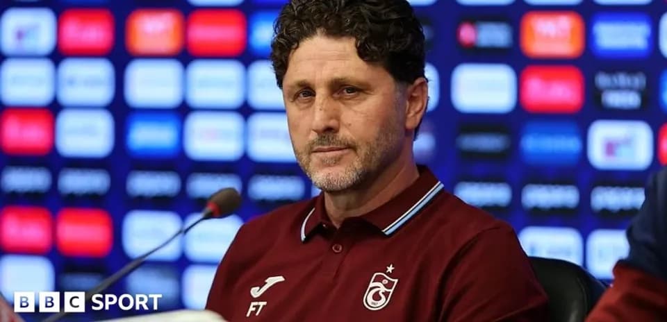 Manager speaking at press conference with logos in background