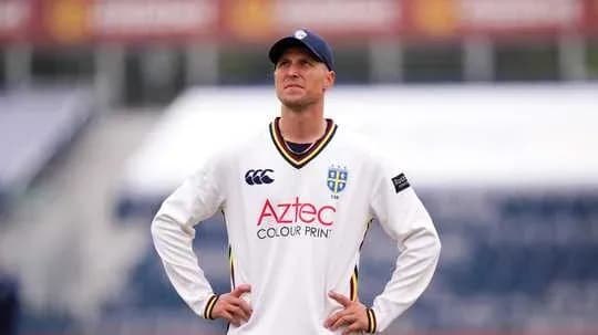 Cricketer in white kit looking upwards on field