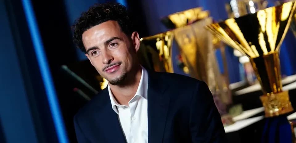 Man in suit posing with trophies in background