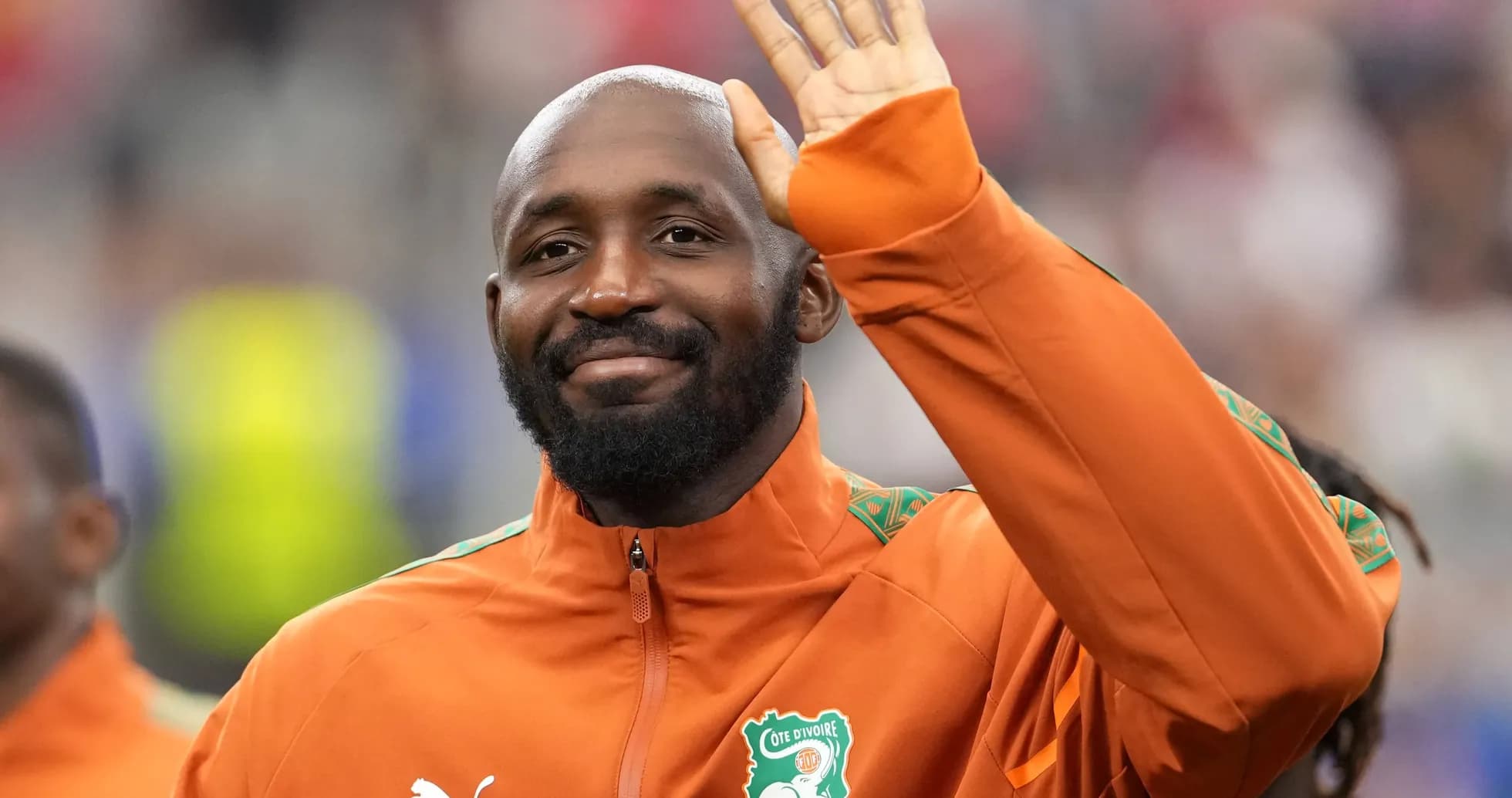 Player waving during pre-match ceremony in orange jacket