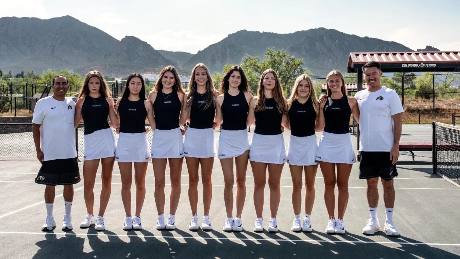 Tennis team posing on court with coaches