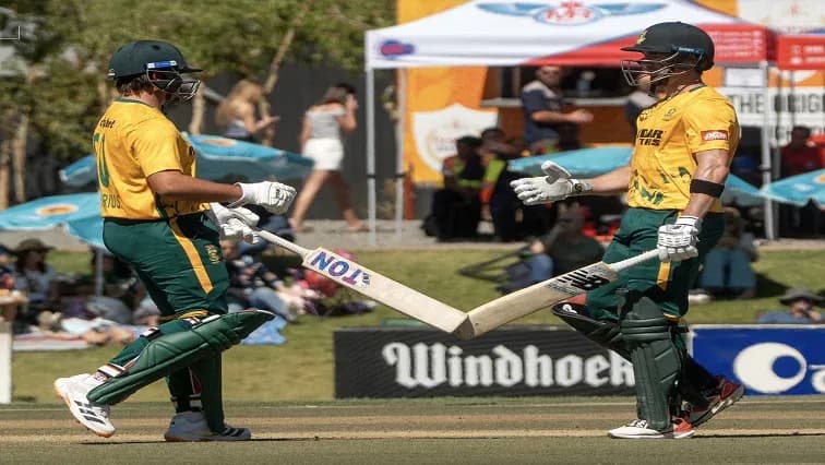 Two cricketers exchanging bats during match celebration