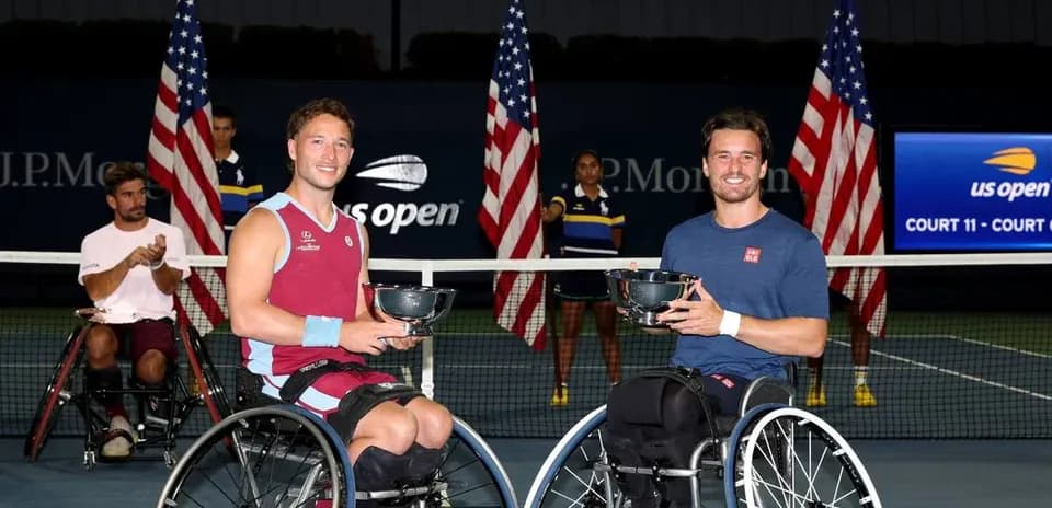 Two wheelchair tennis players holding trophies on court