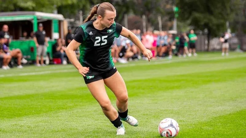 Player in black uniform kicking soccer ball on field Player in black uniform kicking soccer ball on field
